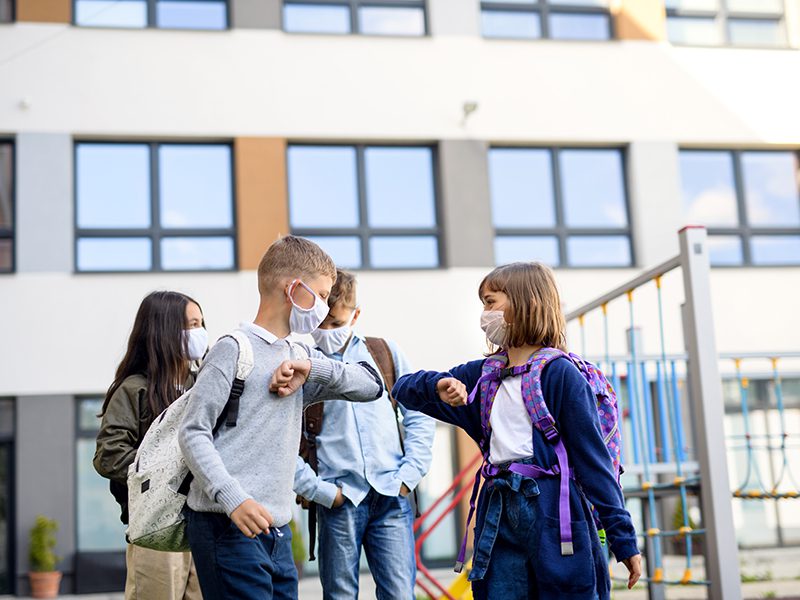 Kids saying goodbye with elbows while wearing masks at school